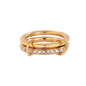Könnte beinhalten: Ein Satz von drei goldfarbenen Ringen. Ein Ring ist ein schlichtes Band, ein anderer ein Band mit klaren Kristallen, und der dritte Ring ist ein schlichtes Band. Die Ringe sind mit goldfarbenen Verbindern verbunden.