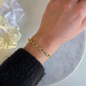 Könnte beinhalten: Ein goldenes Kettenarmband mit kleinen, klaren Steinen, die in die Glieder eingefasst sind. Das Armband befindet sich an einem Handgelenk.