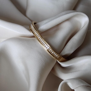 Könnte beinhalten: Ein goldenes Armreif-Armband mit einer Reihe von klaren Zirkonia-Steinen.