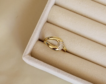 May include: A gold-colored ring with a unique design. The ring features a split band and a curved, open center. The center section is adorned with small, sparkling stones, adding a touch of elegance to the jewelry.
