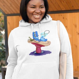 以下が含まれることがあります： 白いフード付きスウェットシャツに、不思議の国のアリスの青いイモムシがキノコの上で水タバコを吸っているグラフィックがプリントされています。