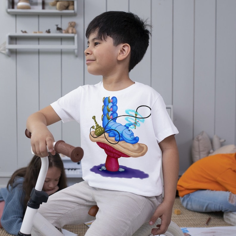 以下が含まれることがあります： アリス・イン・ワンダーランドの青いイモムシのキャラクターがキノコに座っている白いTシャツ。イモムシは水パイプを吸っていて、青と白のストライプの体をしている。