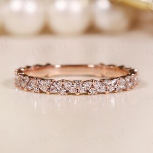 May include: A rose gold band ring featuring a continuous row of marquise-cut and round-cut clear stones set in a leaf-like pattern. The metal has a warm, metallic finish, and the stones are arranged to create a repeating, symmetrical design.