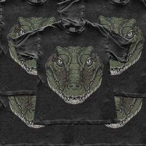 Peut inclure: Un t-shirt à manches courtes noir anthracite présentant une grande impression graphique détaillée d'une tête de crocodile verte centrée sur le devant. L'illustration du crocodile montre des écailles texturées, des dents acérées et des yeux concentrés.