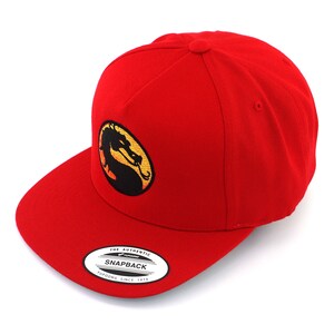 May include: Red baseball cap with a black and yellow embroidered dragon logo. The logo is a circle with a dragon inside. The cap has a curved brim and a snap closure. The text "THE AUTHENTIC SNAPBACK YUPOONG SINCE 1974" is on a white tag attached to the cap.