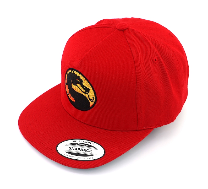 May include: Red baseball cap with a black and yellow embroidered dragon logo. The logo is a circle with a dragon inside. The cap has a curved brim and a snap closure. The text "THE AUTHENTIC SNAPBACK YUPOONG SINCE 1974" is on a white tag attached to the cap.