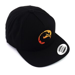 May include: Black baseball cap with a yellow, orange, and red embroidered dragon logo. The logo is in a circle and the text "The Authentic Snapback" is on the back of the cap.
