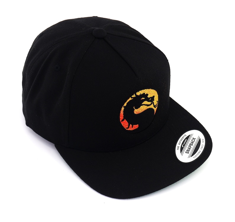 May include: Black baseball cap with a yellow, orange, and red embroidered dragon logo. The logo is in a circle and the text "The Authentic Snapback" is on the back of the cap.