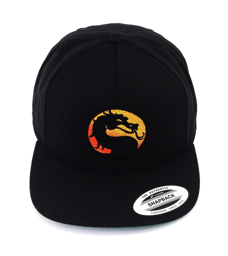 May include: Black baseball cap with a yellow and orange dragon logo embroidered on the front. The logo is a circle with a dragon inside. The cap has a green underside and a white sticker on the back that says "The Authentic Yupoong Snapback Since 1974".