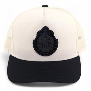 May include: A white and black baseball cap with a mesh back. The front of the cap features a black emblem with text and a design. The brim is black, and the top button is black.