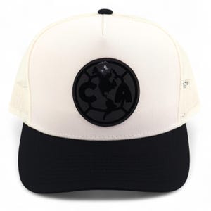 May include: A baseball cap with a black brim and a white mesh back. The front features a black circular emblem with the letters "CA" and a globe design. The top button is black.