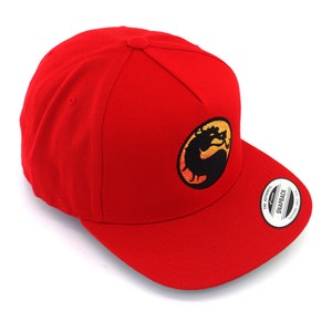 May include: Red baseball cap with a black and orange embroidered logo of a dragon in a circle. The logo says "Snapback" on the back of the cap.