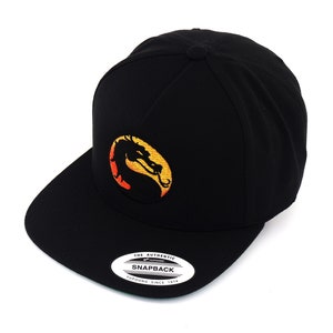 May include: Black and yellow embroidered snapback hat with a dragon logo. The hat has a curved brim and a snap closure. The text "The Authentic Snapback" and "Yupoong Since 1974" is printed on a white tag.