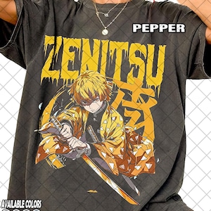 Pode incluir: T-shirt cinza escuro com um gráfico amarelo do personagem Zenitsu do anime. O design inclui o nome do personagem e texto japonês em amarelo. A camisa também mostra as cores disponíveis.