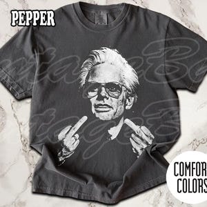 May include: Dark grey t-shirt featuring a black and white graphic of a man wearing sunglasses and giving the middle finger with both hands. The word "PEPPER" is printed at the top left. The shirt is a Comfort Colors brand.
