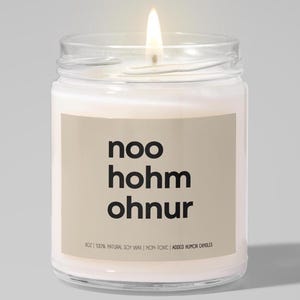 May include: A white candle in a glass jar with a beige label that reads "noo hohm ohnur" and "902 100% NATURAL, SOY WAX | NON-TOXIC | ADDED HUMOR CANDLES".