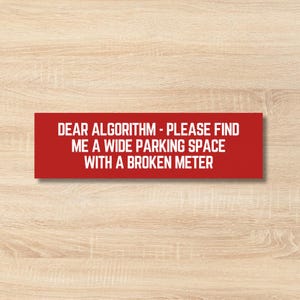 May include: A red rectangular sticker with white text. The text says: "DEAR ALGORITHM - PLEASE FIND ME A WIDE PARKING SPACE WITH A BROKEN METER." The sticker is on a light brown wooden surface.