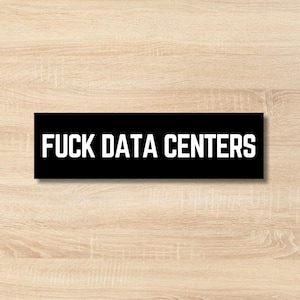 May include: A black rectangular sticker with the white text "FUCK DATA CENTERS". The sticker is placed on a light brown wooden surface.
