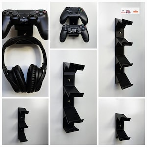 May include: A black wall-mounted gaming headset and controller holder with three slots for controllers. The holder is made of plastic and has a sleek, modern design.