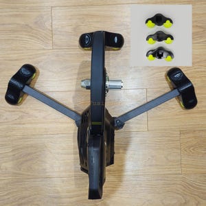 May include: Black bike trainer with a wheel and four black and yellow foot pads. The trainer is on a wooden floor.