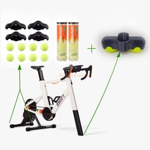 Pode incluir: Uma bicicleta de exercício estática branca e preta com um logotipo laranja que diz "ZWIFT". A bicicleta está em um suporte preto com uma manivela preta e laranja. Duas latas de bolas de tênis estão no lado esquerdo da imagem. As latas são etiquetadas como "HEAD RADICAL". Um suporte de guidão de bicicleta preto e cinza com duas rodas de borracha amarelas está no lado direito da imagem.
