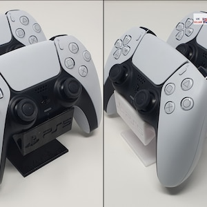 May include: Two white PlayStation 5 DualSense controllers are displayed on a black stand with the PlayStation logo. The controllers are in a vertical position with the front facing the viewer.