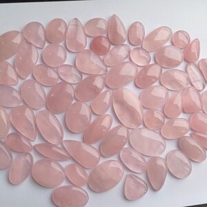 May include: A collection of pink rose quartz cabochons, a type of gemstone, in various sizes and shapes. The cabochons are smooth and polished, with a translucent appearance.