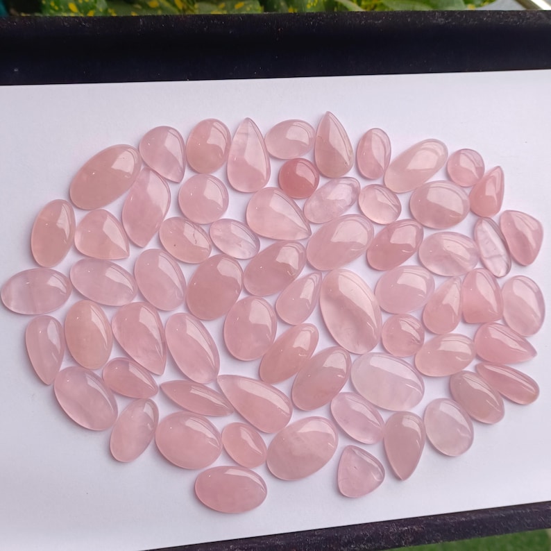 May include: A collection of pink rose quartz cabochons in various sizes and shapes. The cabochons are smooth and polished, with a translucent appearance.