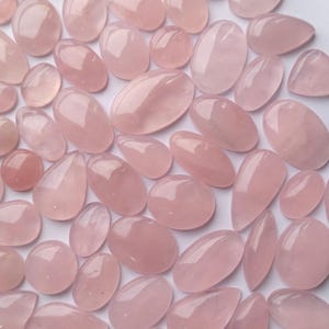 May include: A collection of pink rose quartz stones, each with a unique shape and size. The stones are smooth and polished, with a translucent appearance.