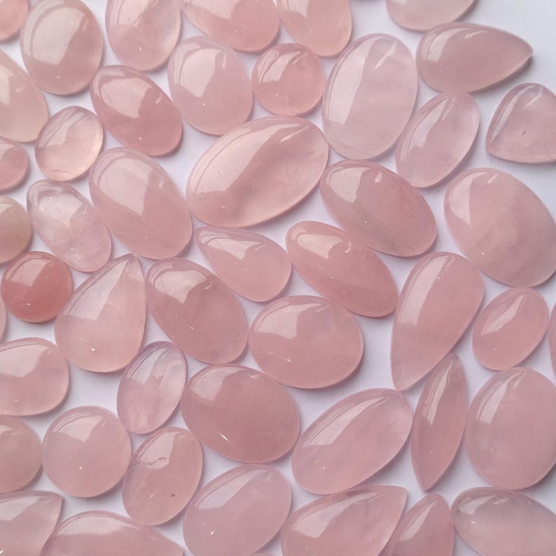 May include: A collection of pink rose quartz stones, each with a unique shape and size. The stones are smooth and polished, with a translucent appearance.