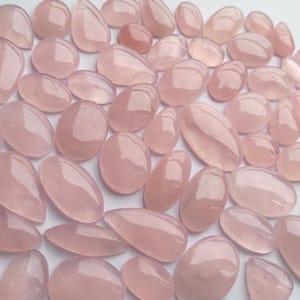 May include: A collection of rose quartz cabochons in various shapes and sizes. The stones are a pale pink color and have a smooth, polished finish.
