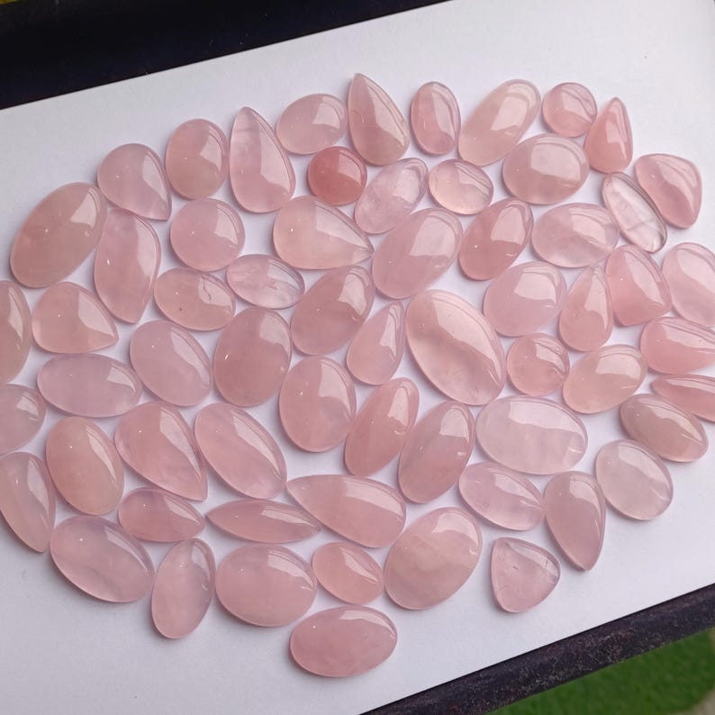 May include: A collection of pink rose quartz cabochons in various sizes and shapes. The cabochons are smooth and polished, with a translucent appearance.