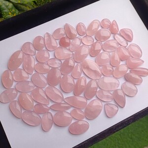 May include: A collection of pink rose quartz cabochons, a type of gemstone, in various sizes and shapes. The cabochons are smooth and polished, with a translucent appearance.