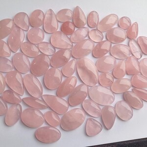 May include: A collection of pink rose quartz cabochons, a type of gemstone, in various shapes and sizes. The stones are smooth and polished, with a translucent appearance.