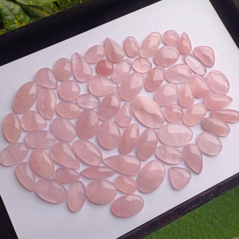 May include: A collection of pink rose quartz cabochons, a type of gemstone, in various sizes and shapes. The cabochons are smooth and polished, with a translucent appearance.