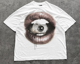 May include: White t-shirt with a graphic print of a large, open mouth with an eye inside. The mouth is pink and the eye is brown.