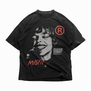 Może przedstawiać: Czarny t-shirt z szarą grafiką uśmiechniętej twarzy. Słowo "MISFIT" jest wydrukowane na czerwono na dole, z czerwonym "R" w okręgu po prawej stronie. Koszulka ma wygląd vintage.