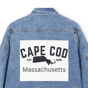 Pode incluir: Uma jaqueta de ganga azul com um remendo branco nas costas que diz "CAPE COD EST. 1620 Massachusetts" com uma silhueta do estado de Massachusetts.