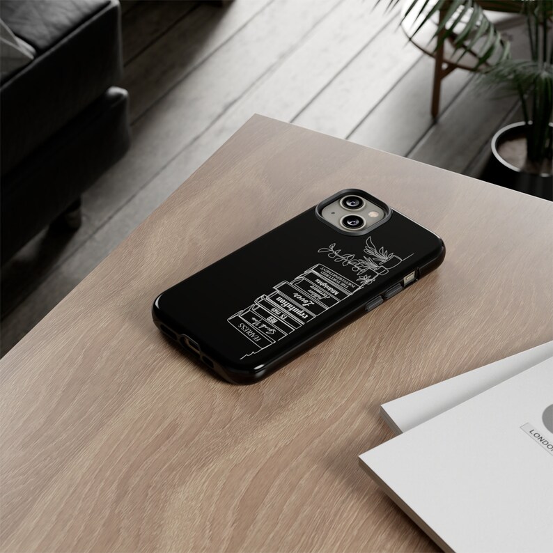 May include: Black phone case with a white outline of a stack of books and a plant. The phone case is for an iPhone 13 Pro Max.