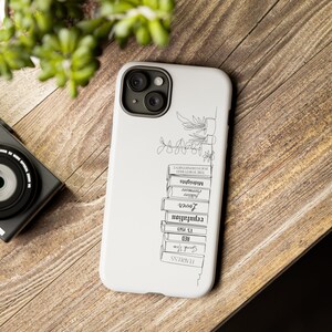 May include: White phone case with a black line drawing of a stack of books with titles like "Fearless", "Red", "12. 1995", "Revolution", "Lover", "Forever", "Covenant", "Midnights", and "The Tormented", with a small plant on top.