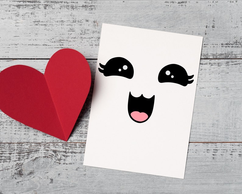 May include: A white card with a black and white cartoon face with big eyes and a wide smile. The card is next to a red paper heart.