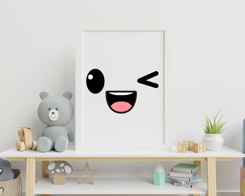 May include: A white framed print with a black and pink cartoon face with a winking eye and a wide smile. The print is hanging on a white wall above a wooden shelf with a teddy bear, a wooden toy, and books.