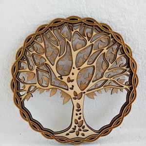 Peut inclure: Un motif d'arbre de vie en bois découpé au laser. L'arbre présente des branches, des feuilles et un tronc texturé détaillés, le tout dans une bordure décorative et superposée. Les tons de bois naturel créent une esthétique chaleureuse, idéale pour la décoration intérieure.