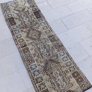 May include: A long, rectangular rug with a beige background and a brown geometric pattern. The rug has a distressed, vintage look.
