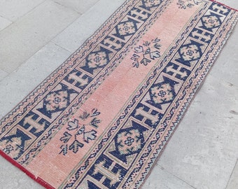 Puede incluir: Una alfombra de color rosa y azul con un diseño geométrico. La alfombra tiene un aspecto descolorido y vintage y está hecha de tejido tejido.
