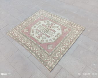 Puede incluir: Alfombra cuadrada vintage con un diseño geométrico central en crema, rosa y verde apagado. La alfombra presenta un borde detallado y un patrón simétrico, adecuada para la decoración del hogar.