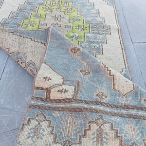 May include: A rectangular runner rug featuring a light blue, cream, and lime green geometric pattern. The rug is partially folded over, revealing a textured weave and a fringed edge. The text REDMI 12 and 18/10/2026 17:17 is visible.