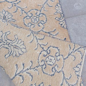 May include: A beige rug with a blue floral pattern. The rug is woven with a textured surface and has a fringed edge.