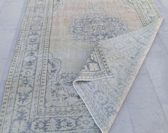 May include: A light green and cream vintage rug with a faded floral pattern and a dark blue border. The rug is folded in half and is lying on a light grey tiled floor.