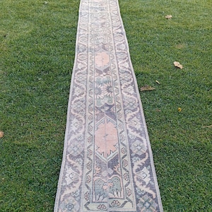 Peut inclure: Un tapis long et rectangulaire avec un motif persan traditionnel. Le tapis est dans des tons de rose, vert et marron, et a une frange blanche sur les bords.